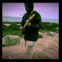 a man holding a guitar in front of the ocean